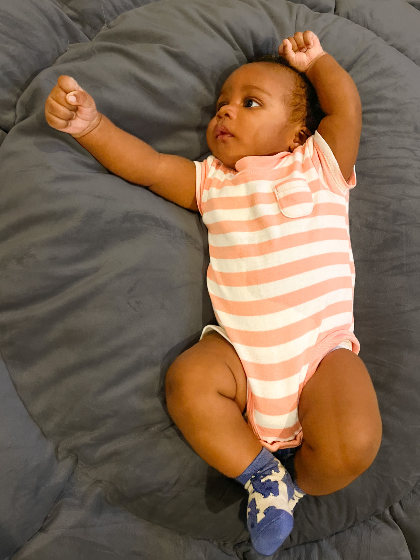 OLUWAFIREJIMI CHUKWUDEZIRI (FJ) ASUGHA as a baby, stretching his arms in a striped bodysuit